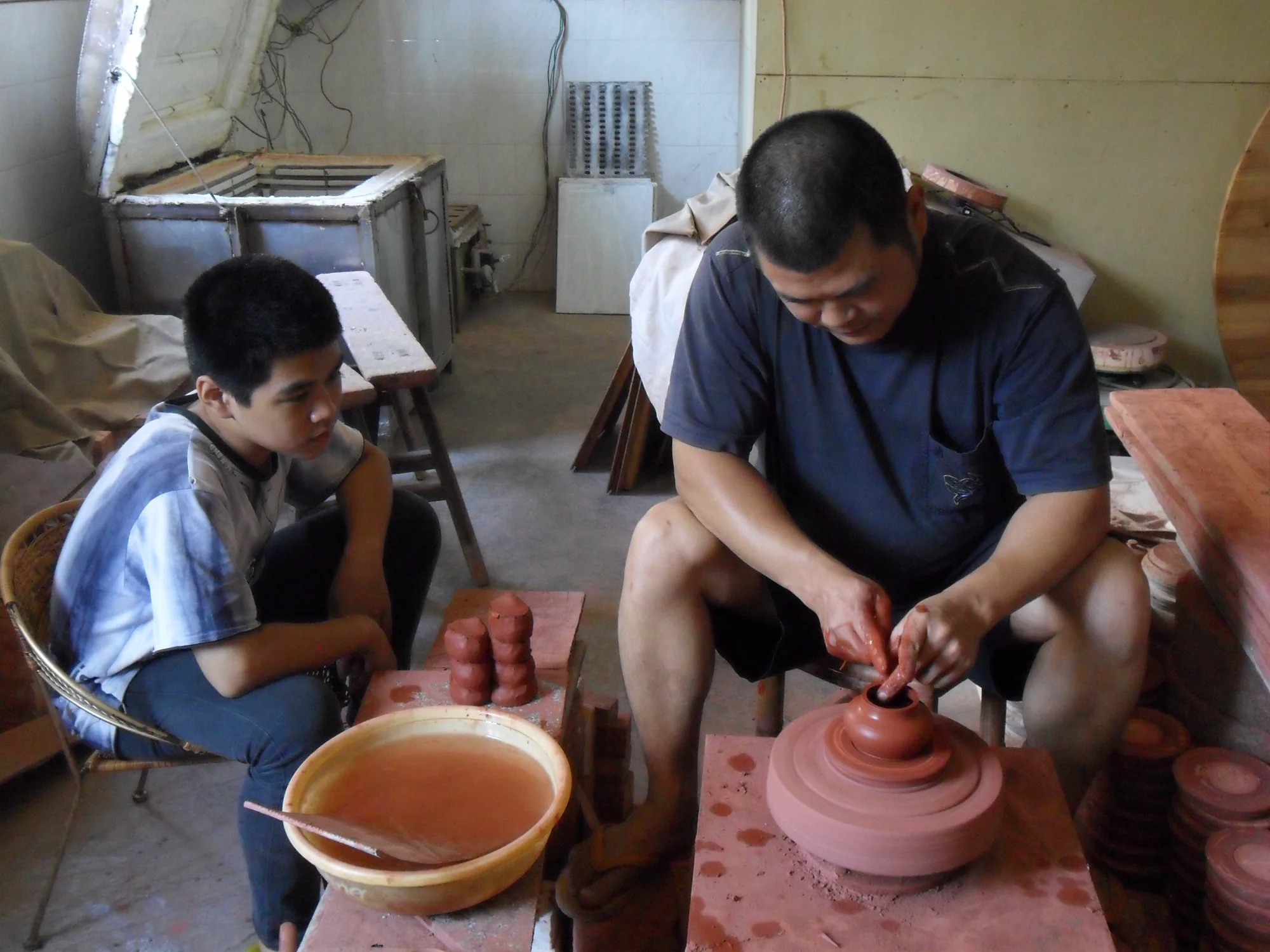 Zhang Jincai demonstrating hand-pulled red-clay teapot making beside the pottery wheel