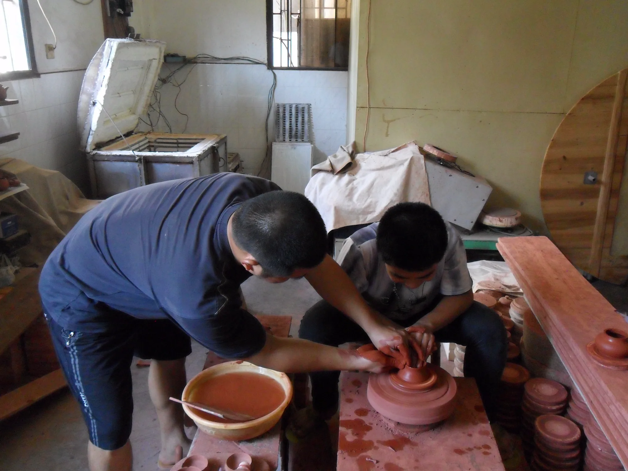 Zhang Jincai supporting the clay body and demonstrating hand position beside the pottery wheel