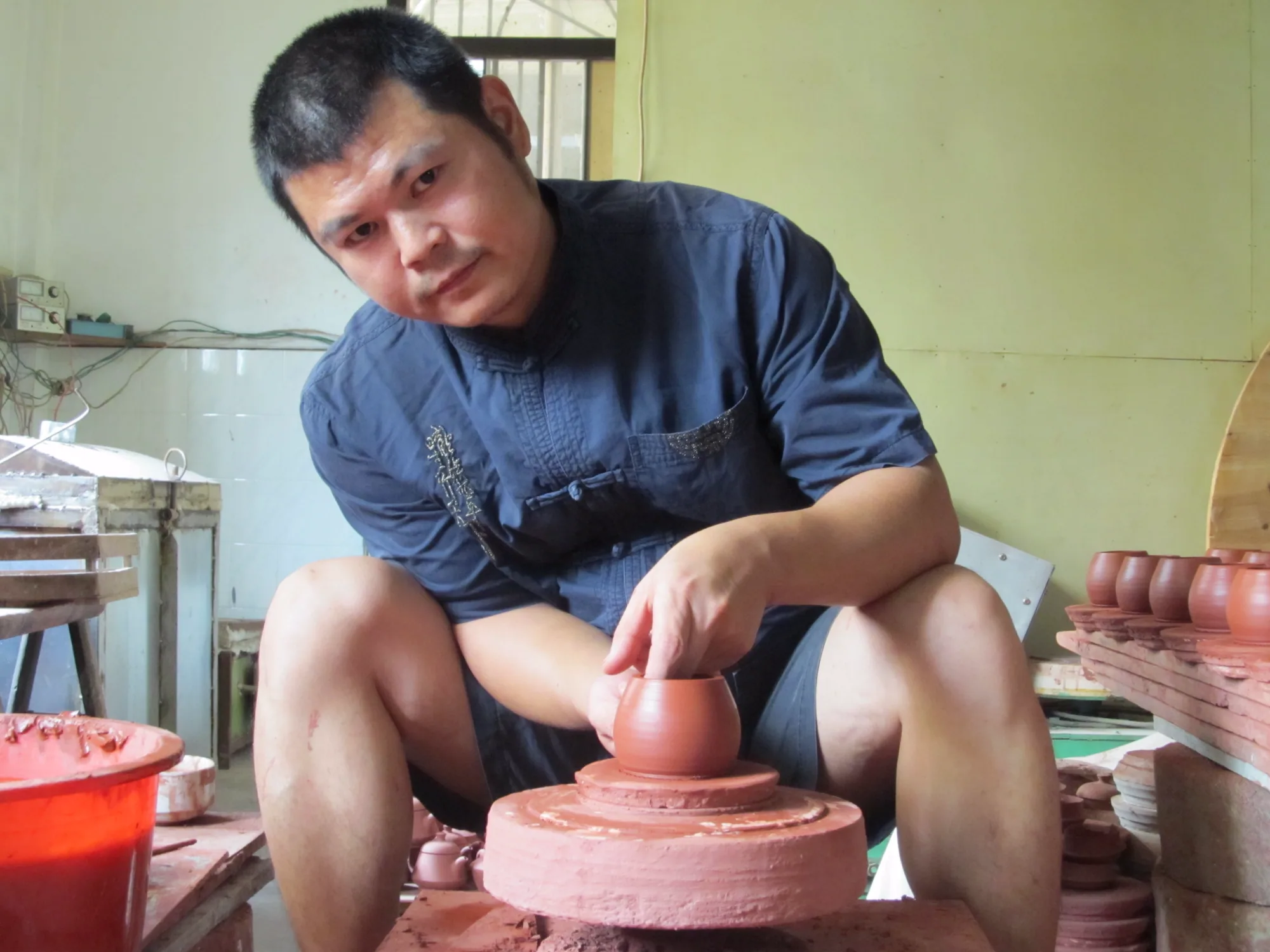 Zhang Jincai refining the form of a hand-pulled red-clay vessel