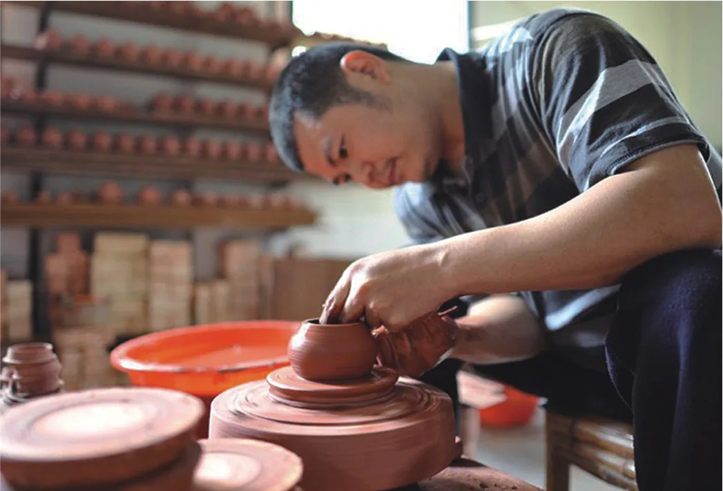Zhang Jincai working at the wheel with rows of red-clay forms behind him